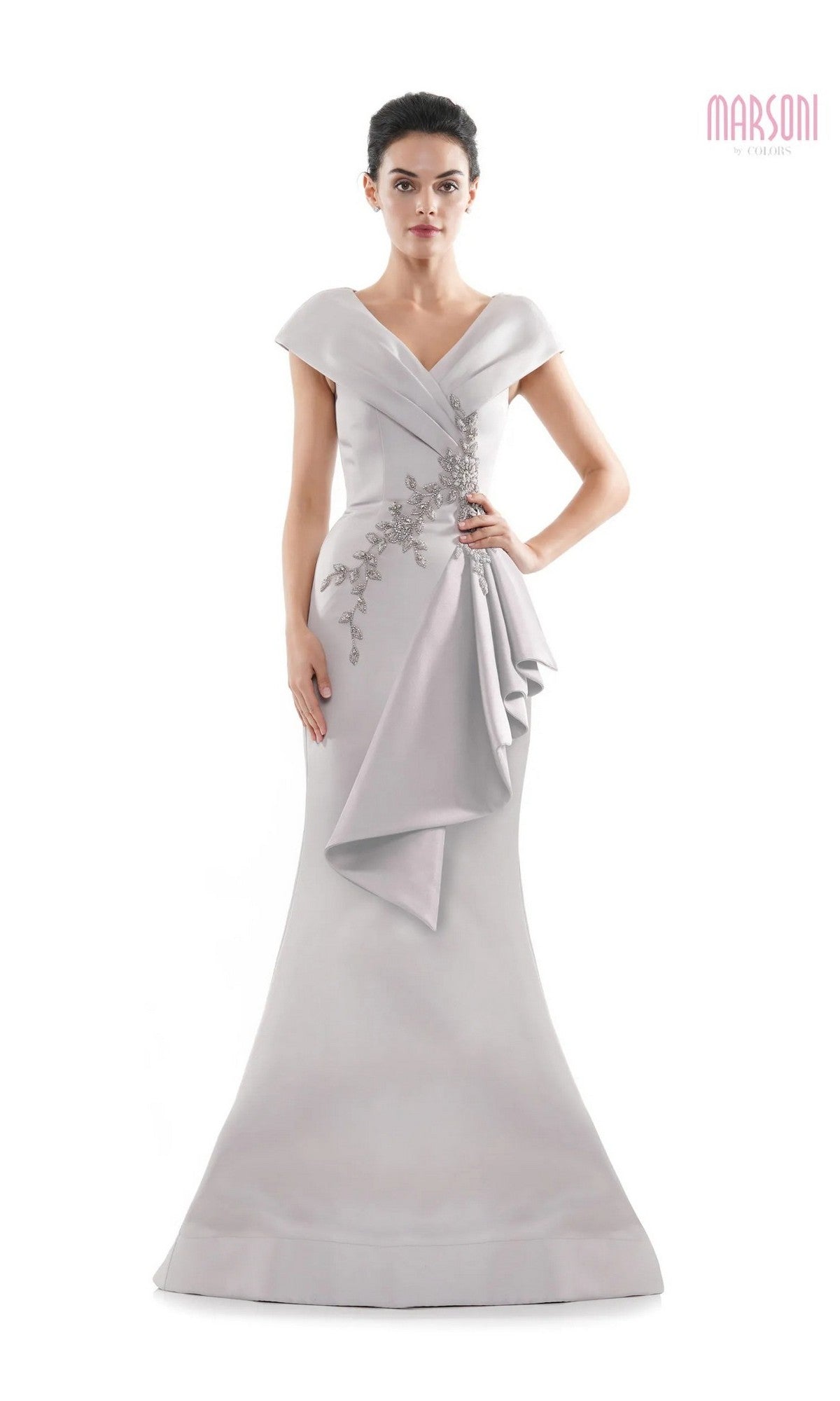 A woman wears the Long Formal Dress: Marsoni MV1086 in taupe, featuring cap sleeves, beaded embellishments, and draped detailing, as she stands against a white background. The Marsoni logo is displayed in the top right corner.
